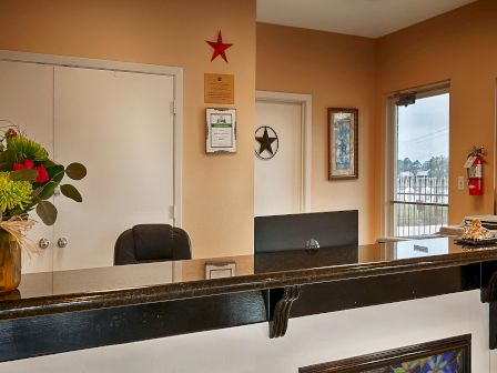 This image shows a reception desk with a floral arrangement, a black chair, wall decor, windows, and a door in the background, ending the sentence.