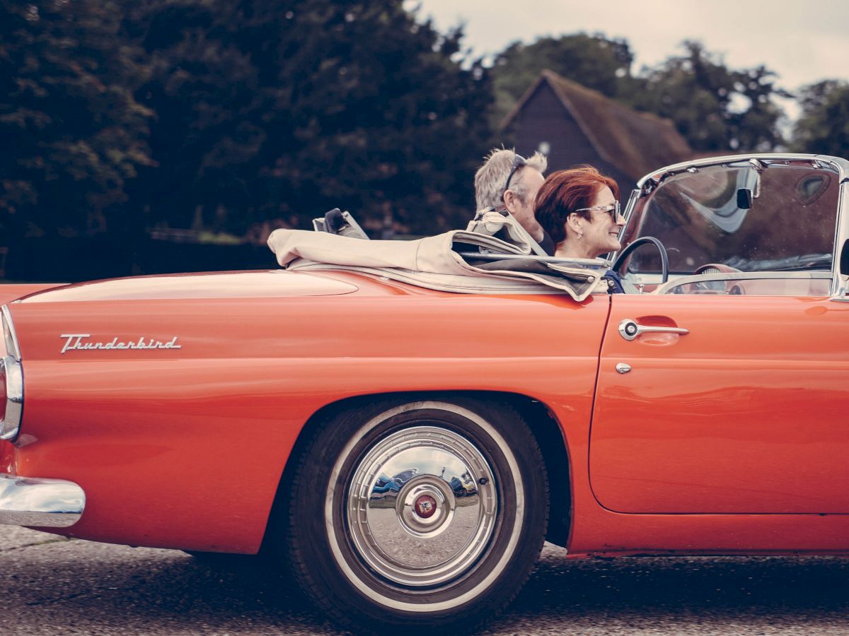 Two individuals are enjoying a ride in a classic, red convertible car with the word 