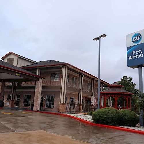 The image shows a Best Western hotel with a prominent sign, a covered entrance, and a small gazebo surrounded by greenery.