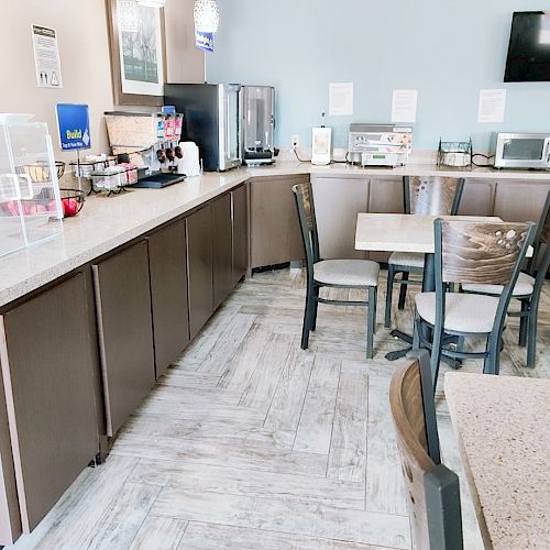 This image shows a small dining area with a counter holding beverage and food dispensers, tables, chairs, a microwave, and a fridge.