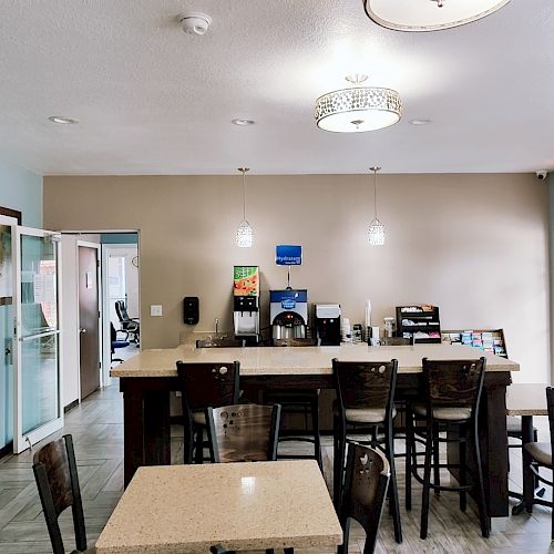 A modern dining area with tables, chairs, coffee machine, and snack station with pendant lights hanging from the ceiling.