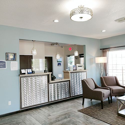 The image shows a modern reception area with a check-in counter, chairs, a lamp, a window, and wall decor, creating a welcoming atmosphere.