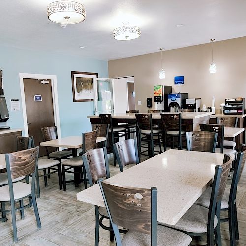 The image shows a dining area with tables, chairs, a flat-screen TV, a microwave, a coffee station, and a stand with brochures.