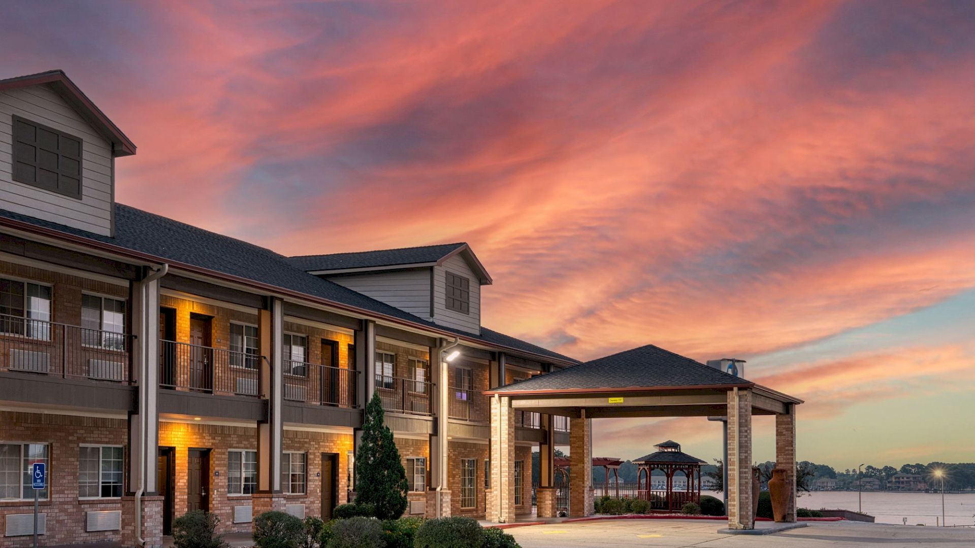 A modern apartment complex by the water at sunset, with warm lights glowing and a colorful pink-orange sky overhead.