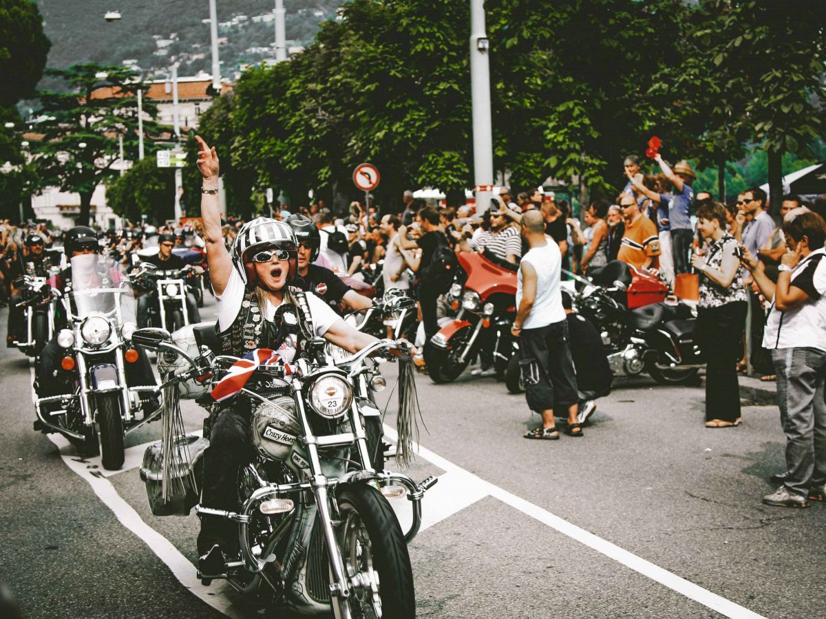 A group of motorcyclists rides down a street while a crowd of people stands on the sides, cheering and taking photos, ending the sentence.