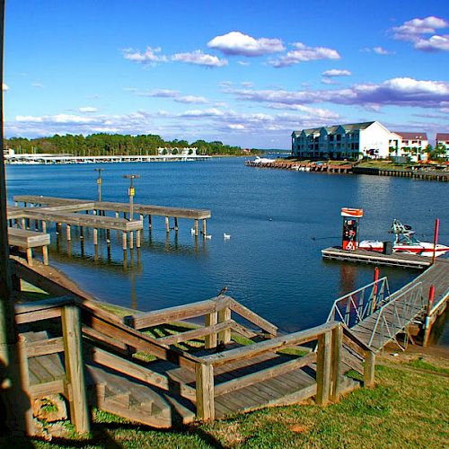 The image shows a waterfront scene with a wooden dock, some buildings across the water, and a small boat docked. The sky is partly cloudy.