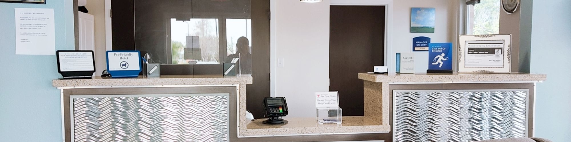 This image shows a reception area with a modern design, featuring a desk with decorative panels, pendant lights, and a seating area.